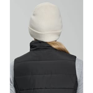 A cream beanie with a ribbed design, worn by a person in a black vest. The back of the beanie is visible.