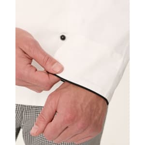 A close-up of a white executive chef jacket featuring black piping, highlighting the cuff detail and button.