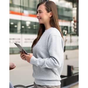 A grey crew fleece jumper, featuring a relaxed fit and long sleeves, is worn by a woman holding a tablet.