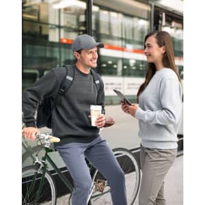 A grey crew fleece sweat worn by a woman and a dark grey version on a man, both casually styled outdoors with bicycles.