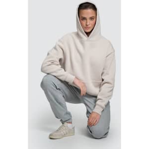 A unisex premium fleece oversized hoodie in light grey, worn by a model with grey tracksuit bottoms and sneakers.