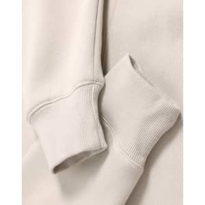 A close-up of a beige oversized hoodie featuring ribbed cuffs and a soft fleece texture. It has a logo.