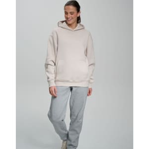An oversized hoodie in a light beige colour, featuring a front pocket and a hood, paired with grey sweatpants.