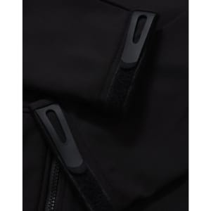 Close-up of a black softshell jacket featuring zippers and velcro details. The jacket has a logo on it.