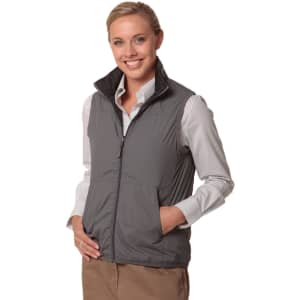 A woman in a grey versatile vest with a zip, paired with a striped shirt, smiling and standing with hands by her side.