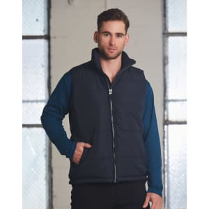 A heavy quilted vest in navy blue, featuring a front zip and side pockets, worn over a long-sleeve top.