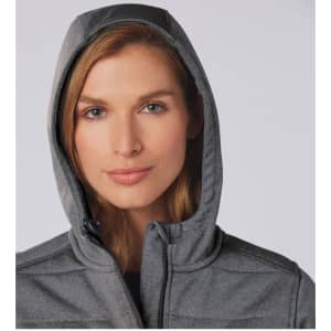 A close-up of a woman wearing a grey padded jacket with a hood. The jacket features a logo.