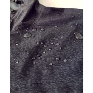 A close-up of a dark grey waterproof jacket with water droplets on the fabric and a hood. The jacket has a logo.