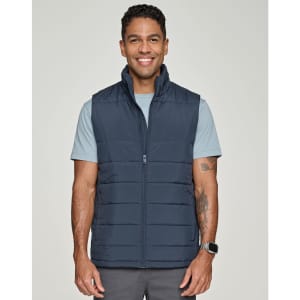 A man wearing a navy blue insulated puffer vest over a light blue shirt, smiling at the camera.