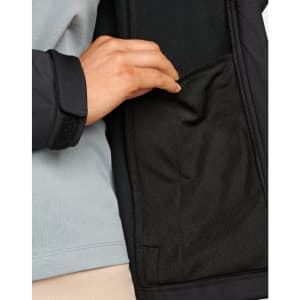A close-up of a hand reaching into the interior pocket of a black softshell jacket.