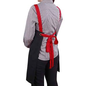 A black canvas bib apron with red straps tied at the back, worn by a person in a checkered shirt.