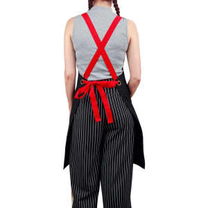A black canvas bib apron with red straps worn over striped pants, featuring a tied waist and a logo on the back.