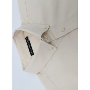 A beige men's long-sleeve shirt featuring a collar and buttons, with a branding label on the inside.