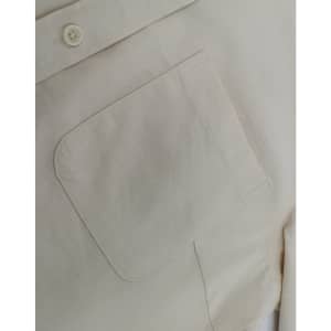 A close-up of a light beige cotton blend long-sleeve shirt, featuring a chest pocket and a button detail.