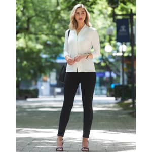 A mid sleeve knit top in white, paired with black leggings, set against a green park backdrop. The model carries a bag.