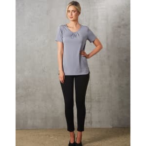 A grey short-sleeve knit top with pleats, paired with black fitted pants, worn by a model against a textured background.