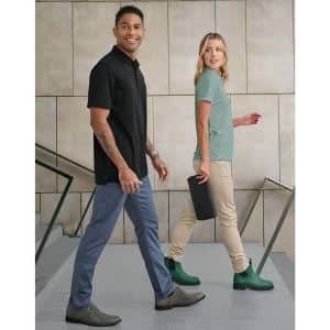 A pair of models walking, wearing black and mint polo shirts, with tan flexi chino pants, and green boots.