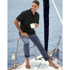 Men's flexi chino pants in navy, modelled by a man on a boat, wearing a black polo and holding a cup.