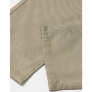 A close-up of khaki chino pants, highlighting the fabric and stitched hem. The image features a logo or branding detail.