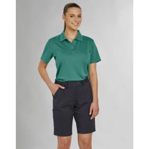 A woman in a teal polo shirt and navy utility cargo shorts, standing confidently with hands in pockets.