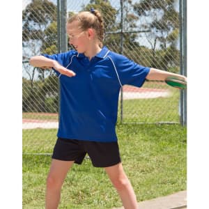 A girl wearing a blue polo shirt and black shorts, posing outdoors near a fence. The shirt features a logo.