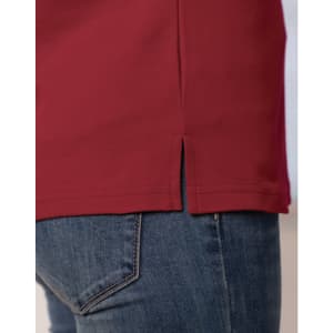 A close-up of a red short sleeve polo shirt featuring side slits, paired with denim jeans. The shirt has a logo.