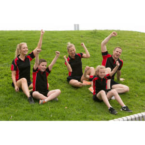 A group of five people wearing black and red polo shirts, celebrating and posing joyfully on green grass.