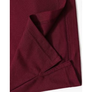 A close-up of the hem and fabric of a burgundy polo shirt, featuring a logo on one side.