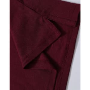 A close-up of a maroon polo shirt showing folded fabric and stitching details. It features a logo on the collar.