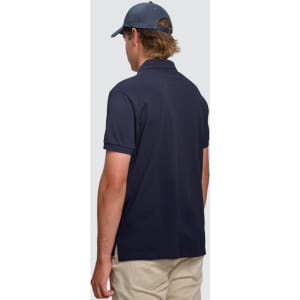 A man wearing a navy ultrafine cotton pique polo shirt, viewed from the back, paired with light-coloured trousers.
