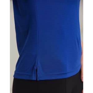 A close-up of a textured polo shirt in vibrant blue, featuring a small slit detail at the hem and a logo.