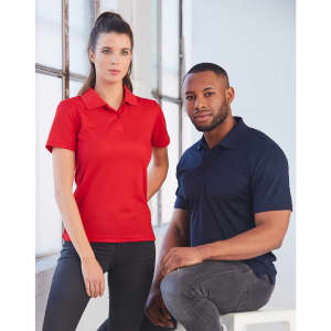 A red women's polo shirt and a navy blue men's polo shirt displayed on models in a bright, modern setting.