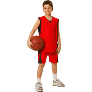 A young boy wearing red basketball shorts and a matching jersey, holding a basketball. The outfit has a logo.