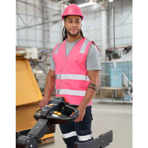 A pink hi-vis safety vest with shoulder reflective tapes, worn by a person in a warehouse setting, featuring a logo.