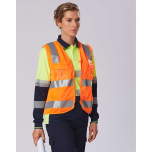 A safety polo shirt in bright yellow and navy with reflective stripes and a logo. A person is wearing it with a safety vest.