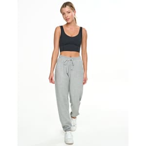 A woman in a black crop top and grey sweatpants stands against a white background. The sweatpants feature a drawstring waist.