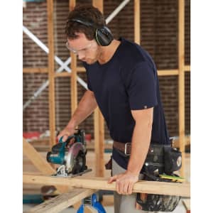A navy blue short-sleeve work t-shirt worn by a man using a circular saw at a construction site.