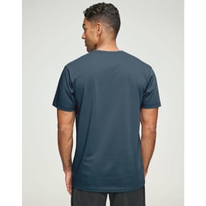 A man is wearing a navy blue premium cotton short-sleeve tee shirt, viewed from the back. The shirt has a logo.