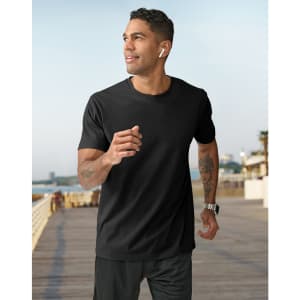 A man in a black short-sleeve tee shirt jogs along a seaside promenade, wearing earbuds and a watch.