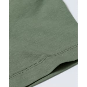 A close-up of a sage green cotton short-sleeve tee shirt featuring a stitched hem and a subtle logo.