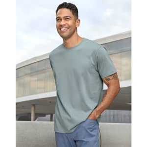 A man wearing a light green premium cotton short-sleeve T-shirt, standing outdoors with a modern building in the background.