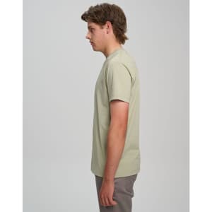 A light green men’s premium cotton t-shirt displayed on a model, viewed from the side. The shirt has a logo on it.