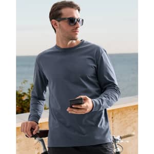 A man wearing a dark blue long-sleeve cotton tee shirt, holding a phone beside a bicycle with a coastal background.