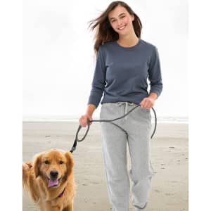 A woman walks a golden retriever on the beach, wearing a dark grey long-sleeve tee and grey sweatpants.