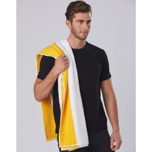 A striped beach towel in yellow and white draped over one shoulder, held by a person wearing a black t-shirt.