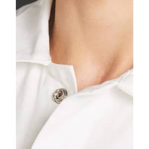 A close-up view of a white collared garment showing a button detail near the neckline. It has a logo.