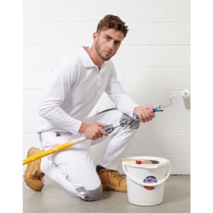 A model kneels in white utility stretch cargo work pants, holding a paint roller and bucket, wearing tan work boots.
