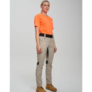 Work pants in beige with black accents, worn by a model in an orange shirt and brown boots, standing against a neutral background.
