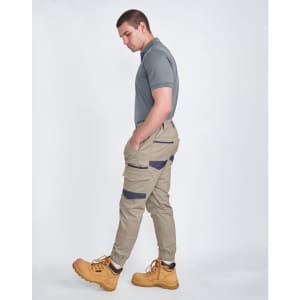 Unisex cotton stretch drill cuffed work pants in light beige with a logo, paired with a grey polo and yellow boots.
