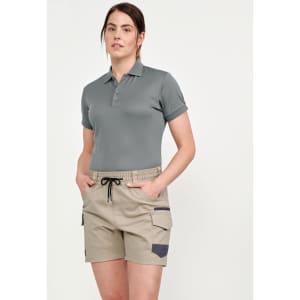 A woman wearing unisex cotton stretch drill shorts in beige, paired with a grey polo shirt. The shorts feature pockets and a drawstring.